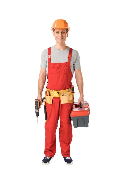 Cheerful construction worker in uniform holding toolbox and drill isolated on white — Stock Photo