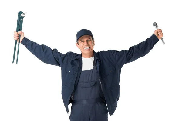 Smiling handyman in overalls holding adjustable wrenches isolated on white — Stock Photo