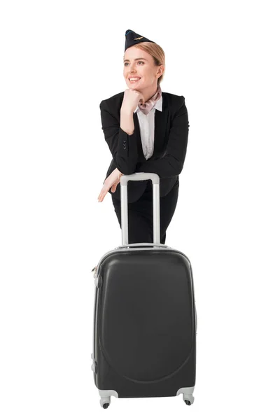 Молода стюардеса в уніформі спирається на валізу ізольовано на білому — стокове фото