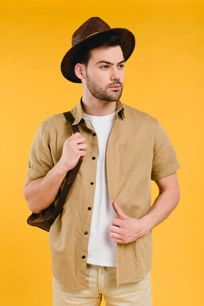 Bärtiger junger Mann mit Hut und Rucksack, der isoliert auf gelbem Grund wegschaut — Stockfoto