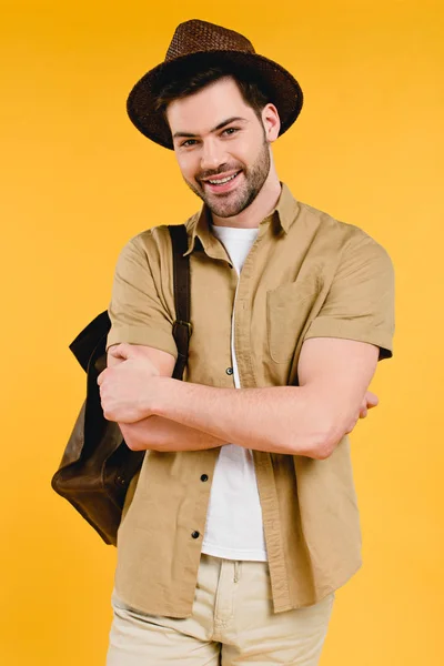 Handsome young man in hat standing with crossed arms and smiling at camera isolated on yellow — Stock Photo