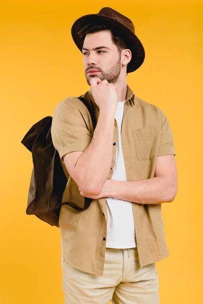Pensive young male traveler standing with hand on chin and looking away isolated on yellow — Stock Photo