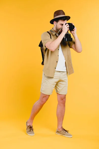 Вигляд на повну довжину молодого чоловіка мандрівника фотографування з камерою ізольовано на жовтому — стокове фото