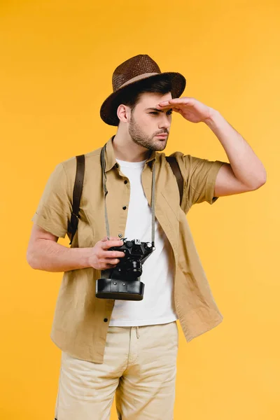 Young male traveler in hat holding camera and looking away isolated on yellow — Stock Photo
