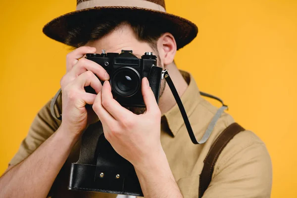 Молодой фотограф фотографирует с камерой, изолированной на желтом — стоковое фото