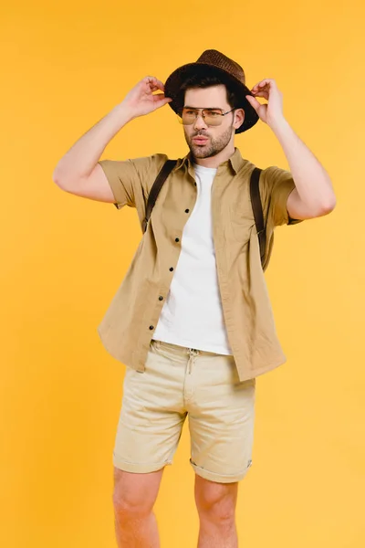 Retrato de jovem bonito em óculos de sol e shorts ajustando chapéu isolado em amarelo — Fotografia de Stock