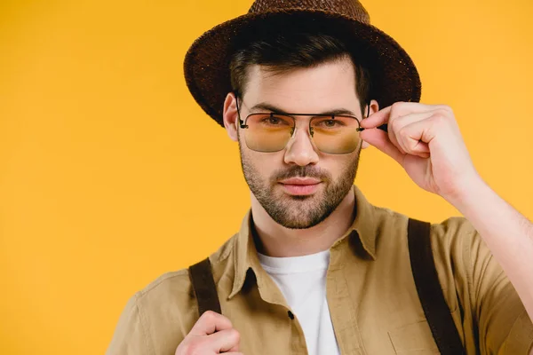 Porträt eines gutaussehenden jungen Mannes mit Hut und Sonnenbrille, der isoliert auf gelb in die Kamera blickt — Stockfoto