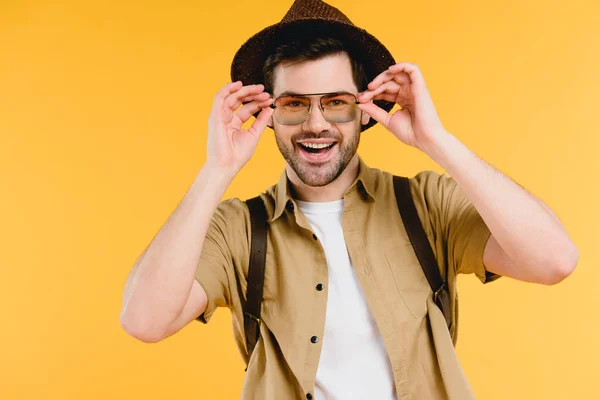 Jovem bonito em chapéu e óculos de sol sorrindo para a câmera isolada no amarelo — Fotografia de Stock