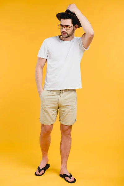 Schöner bärtiger junger Mann in kurzen Hosen und Flipflops, der isoliert auf gelbem Grund wegschaut — Stockfoto