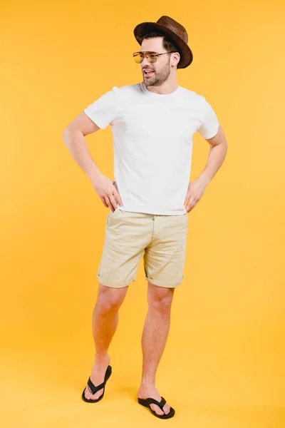 Bello giovane in pantaloncini e infradito sorridente e distogliendo lo sguardo isolato sul giallo — Foto stock