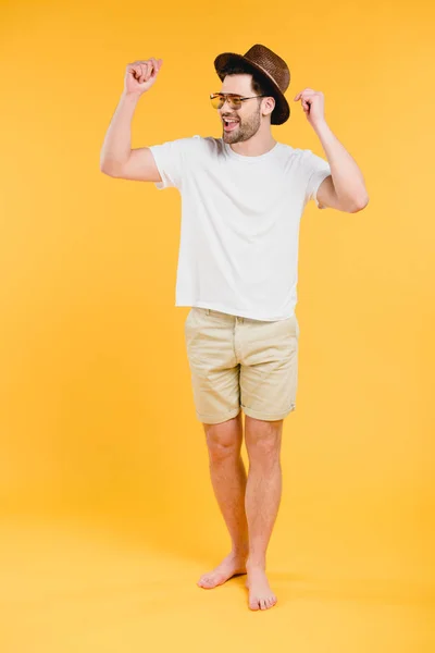 Cheerful young barefoot man in shorts and sunglasses looking away isolated on yellow — Stock Photo