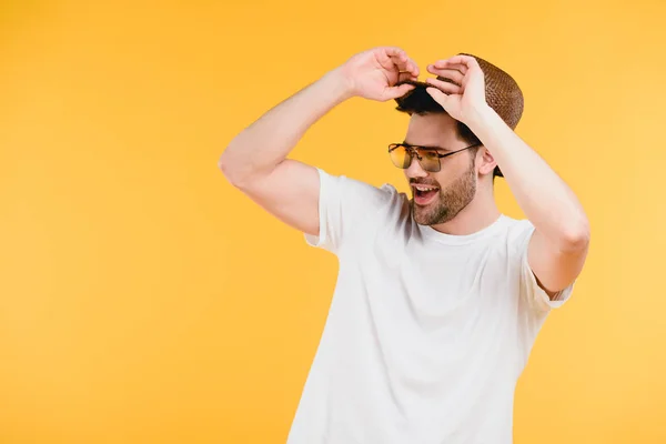 Handsome smiling young man in sunglasses adjusting hat and looking away isolated on yellow — Stock Photo