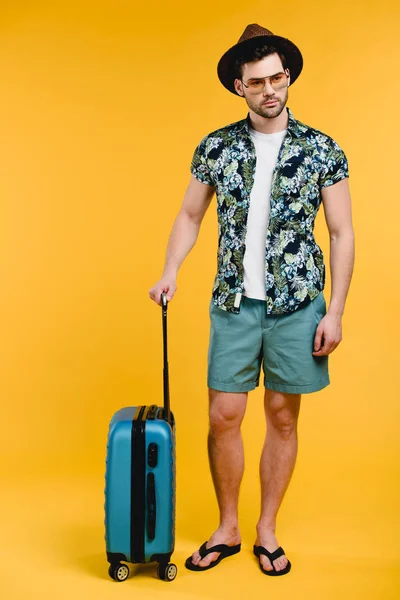 Vista completa de hombre joven guapo en traje de verano sosteniendo maleta aislada en amarillo — Stock Photo