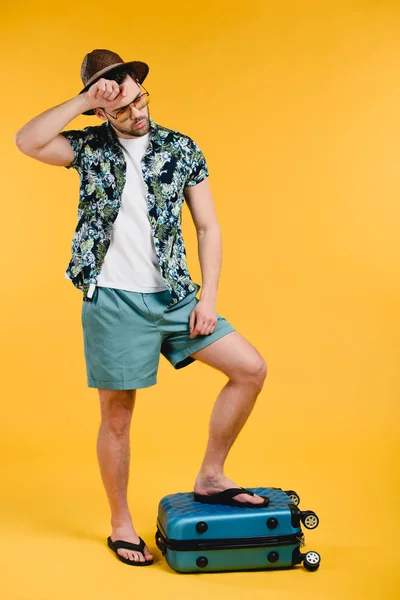 Giovane turista maschio esausto in piedi sulla valigia isolato su giallo — Foto stock