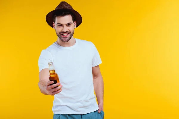 Joven guapo en sombrero sosteniendo botella de vidrio de bebida de verano y sonriendo a la cámara aislado en amarillo - foto de stock