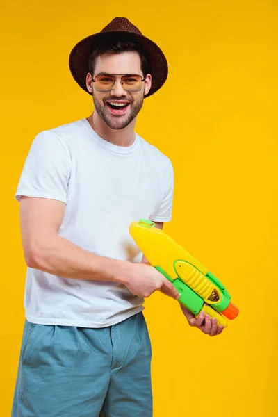 Joven guapo en traje de verano sosteniendo pistola de agua y sonriendo a la cámara aislado en amarillo - foto de stock