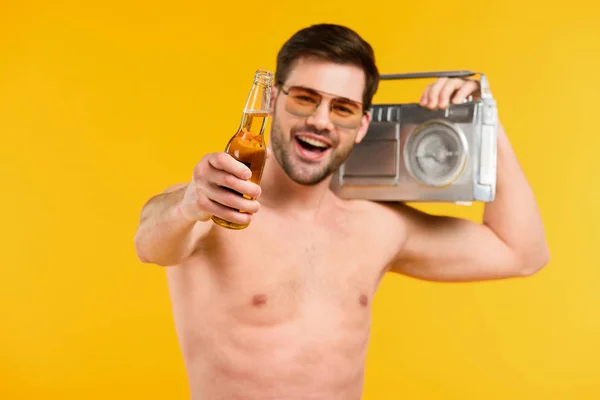 Joyeux jeune homme torse nu dans des lunettes de soleil tenant bouteille de boisson d'été et magnétophone isolé sur jaune — Photo de stock