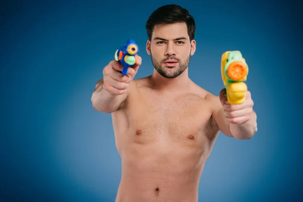 Handsome bearded young man holding water guns and looking at camera on blue — Stock Photo
