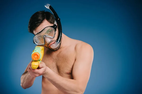 Joven en snorkel y máscara de buceo sosteniendo pistola de agua en azul - foto de stock