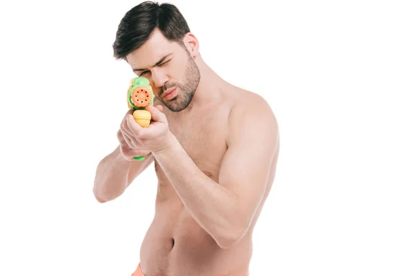 Handsome young shirtless man shooting with water gun isolated on white — Stock Photo