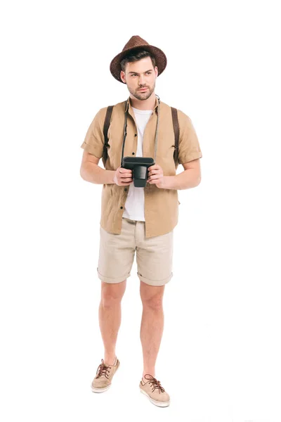 Ganzkörperansicht schöner junger Reisender, der eine Kamera hält und isoliert auf weißem Grund wegschaut — Stockfoto