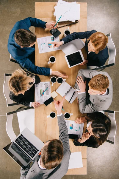 Overhead view of businesspeople on meeting at table with digital devices, coffee cups and documents — Stock Photo