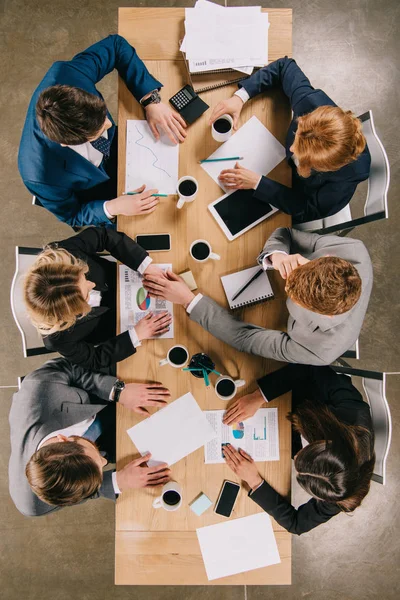 Vista superior de los empresarios discutiendo en la mesa con dispositivos digitales, tazas de café y documentos - foto de stock