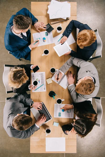 Overhead view of businesspeople discussing at table with digital devices, coffee cups and documents — Stock Photo