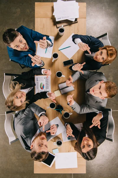 Vue du dessus des collègues d'affaires montrant les doigts du milieu et assis à la table au bureau — Photo de stock