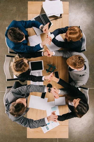 Vue du dessus des gens d'affaires se tenant la main l'un l'autre alors qu'ils étaient assis à table au bureau — Photo de stock