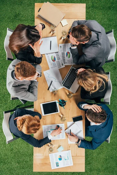 Vue d'ensemble des partenaires commerciaux qui discutent à table avec des documents et des appareils au bureau — Photo de stock