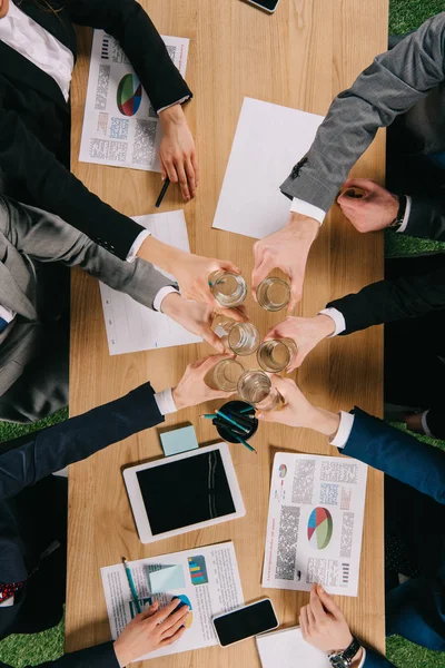 Top view of businesspeople clang glasses together at table in office — Stock Photo