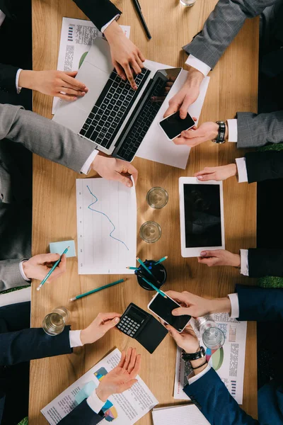 Vista recortada de colegas de negocios mostrando dispositivos digitales entre sí en la mesa en Ofifce - foto de stock