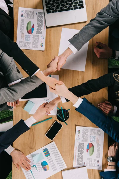 Vista recortada de los socios comerciales estrechando la mano en la mesa en la oficina - foto de stock