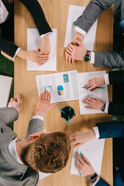 Vista superior del hombre de negocios señalando el diagrama a los socios de negocios en la mesa en la oficina - foto de stock