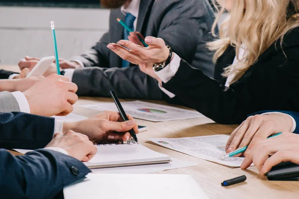 Cropped view of businesswoman gesturing and talking to business colleagues at table in office — Stock Photo