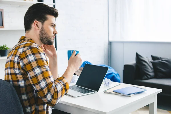 Homme réfléchi buvant du café à la table de travail au bureau à domicile — Photo de stock