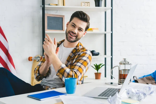 Uomo sorridente seduto al tavolo con laptop in ufficio leggero — Foto stock