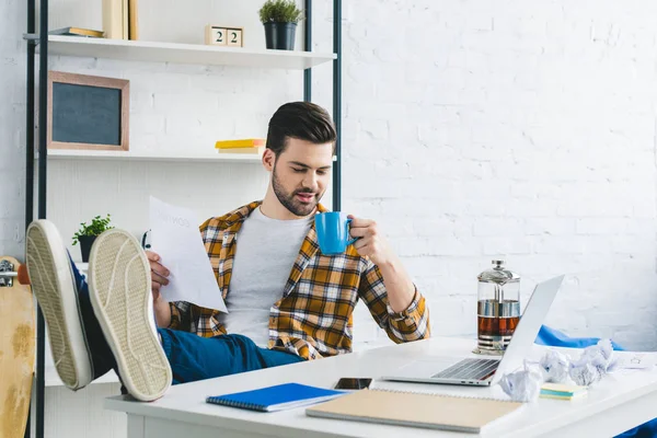 Бизнесмен держит бумагу и пьет кофе в домашнем офисе — стоковое фото
