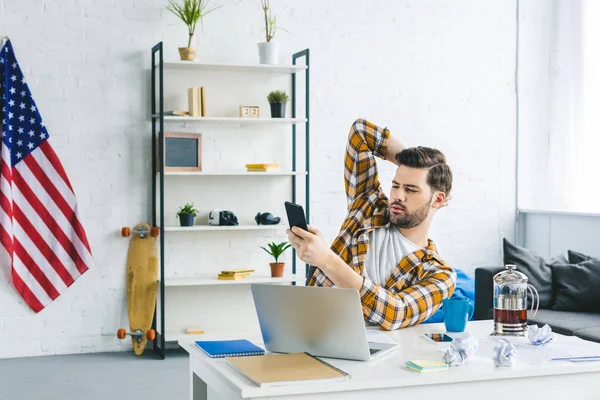 Freelancer working by laptop and holding smartphone in light office — Stock Photo