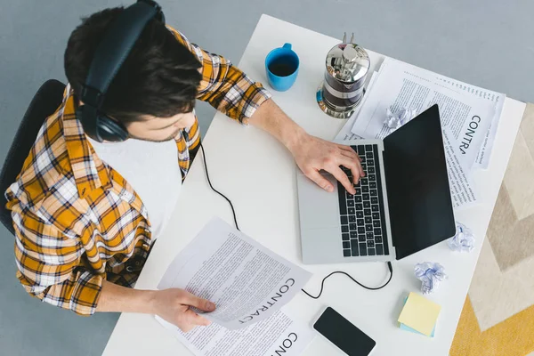 Mann arbeitet am Laptop und hält Auftragspapier im Büro — Stockfoto