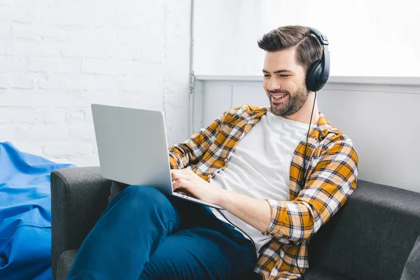 Uomo in cuffia che lavora su laptop in ufficio leggero — Foto stock