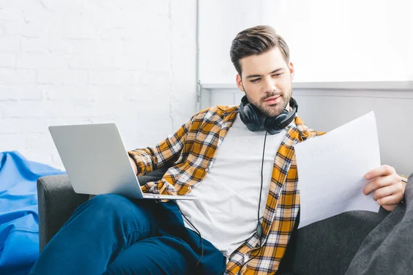 Businessman holing laptop and paper sitting on sofa at home office — Stock Photo