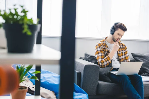 El hombre reflexivo que trabaja en el ordenador portátil en la oficina en casa - foto de stock