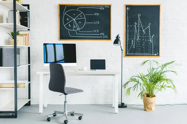 Ordinateurs sur table dans un bureau léger avec des tableaux d'affaires sur les murs — Photo de stock