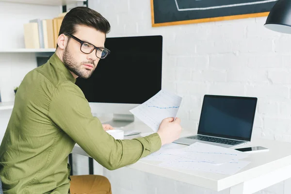 Thoughtful young man by working table with computers at home office — Stock Photo
