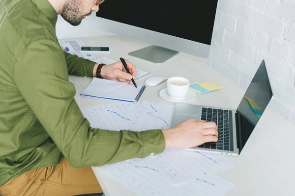 Giovane che lavora al computer e prende appunti a casa — Foto stock