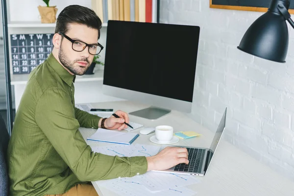 Freelancer in glasses working by laptop in light office — Stock Photo