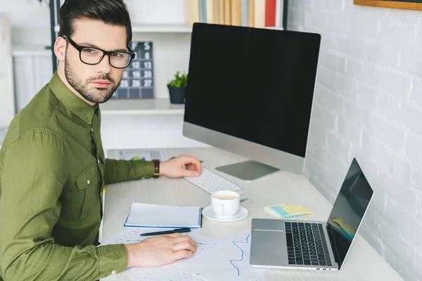 Человек в очках работает за столом с компьютером и ноутбуком в домашнем офисе — стоковое фото