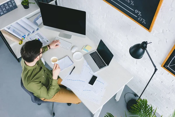 Young businessman working by computer and drinking coffee at home office — Stock Photo